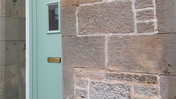 A stone wall with a green door and a wall-mounted light fixture. - Peaceful Country Cottage (Kinghorn)
