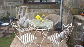 A patio area with wicker furniture, a round table with flowers, and a stone wall. - Peaceful Country Cottage (Kinghorn)