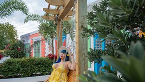 A person in a yellow dress sitting on a wooden swing structure in an outdoor area with a brick floor and greenery. - Hotel Boutique Calizo vip Guest House # 4 (Fajardo)