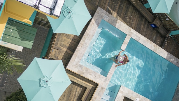 An aerial view of a pool area with multiple umbrellas, a wooden deck, and a person swimming. - Hotel Boutique Calizo vip Guest House # 4 (Fajardo)
