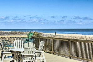 Una terraza de madera con sillas Adirondack y una mesa con vistas a la playa.
