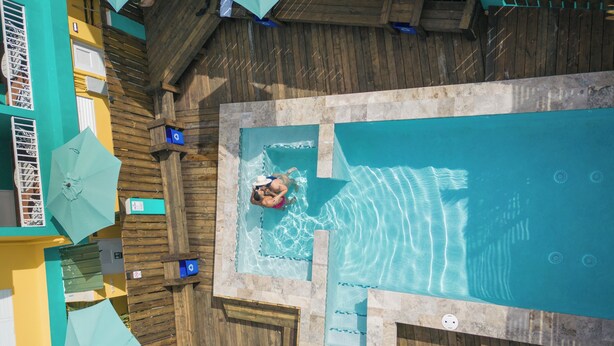A rooftop pool with a wooden deck, a diving board, and a lifeguard chair.