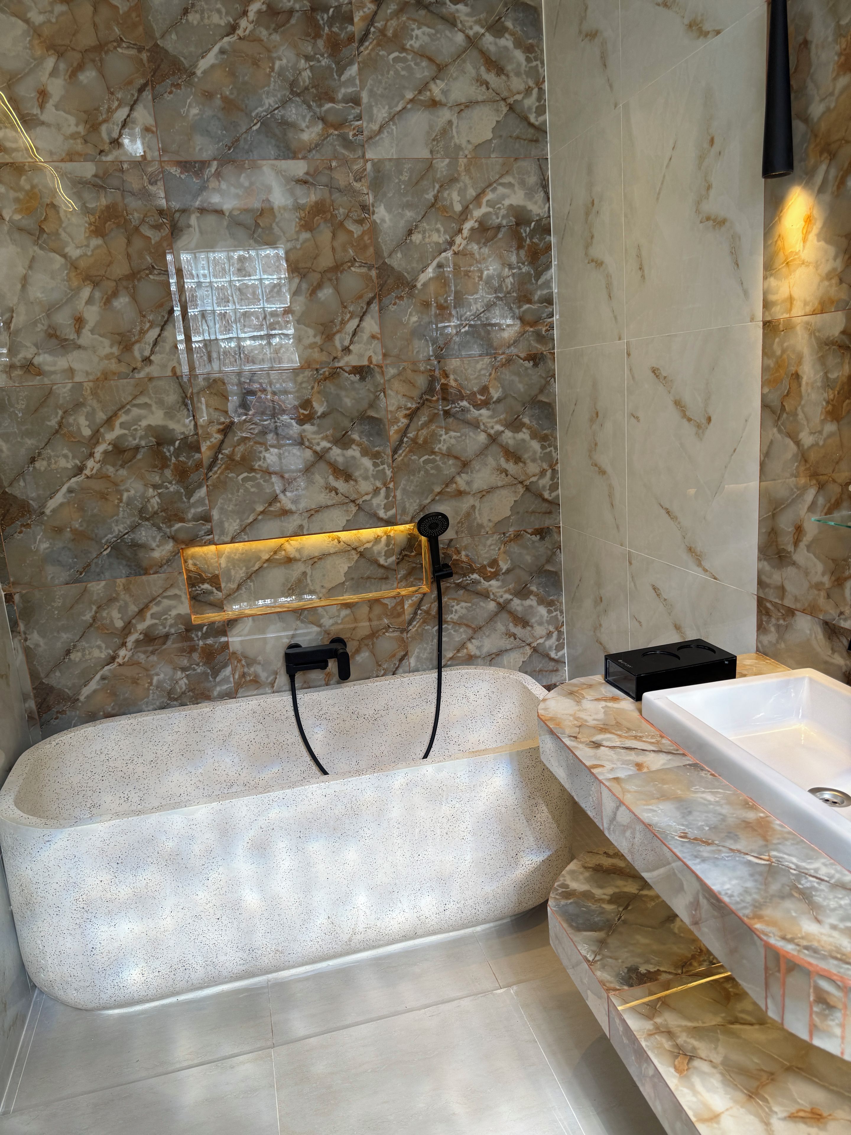 A bathroom with a freestanding bathtub, marble walls, and a modern faucet.