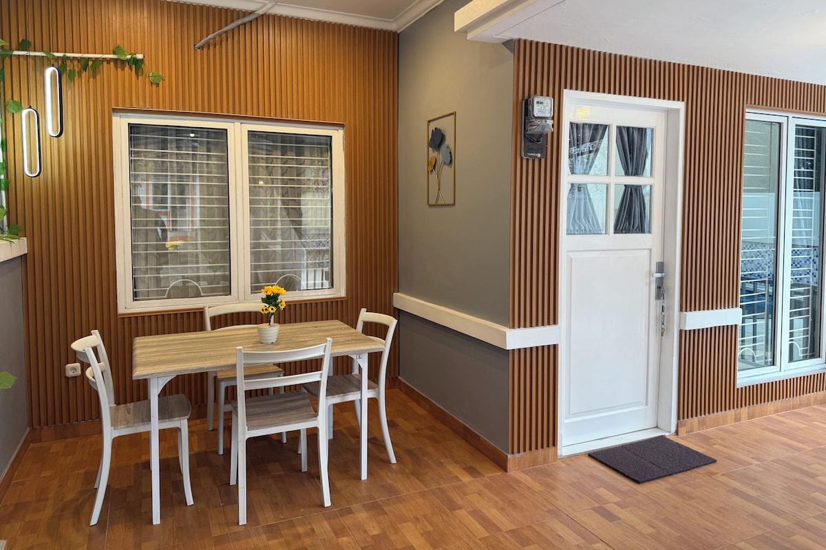 Een eethoek met een houten tafel, witte stoelen en een raam met jaloezieën.