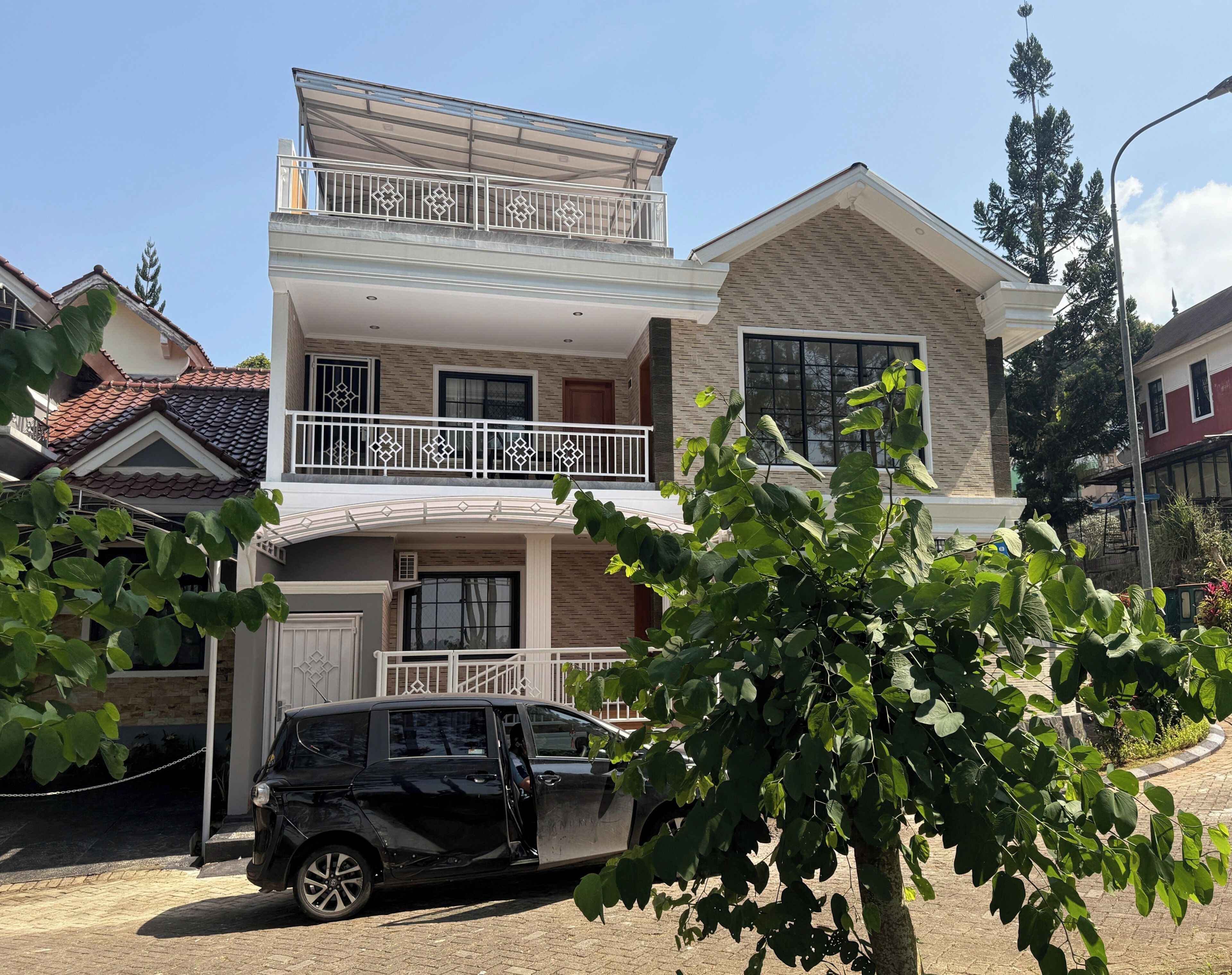 A two-story house with a balcony, a car parked in front, and a tree in the foreground.