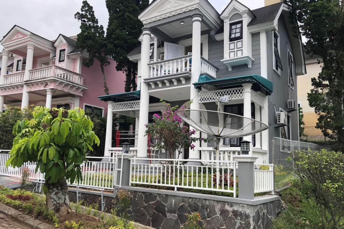 Una hilera de casas de estilo colonial con fachadas blancas y rosas, cimientos de piedra y una cerca de piquetes blancos.