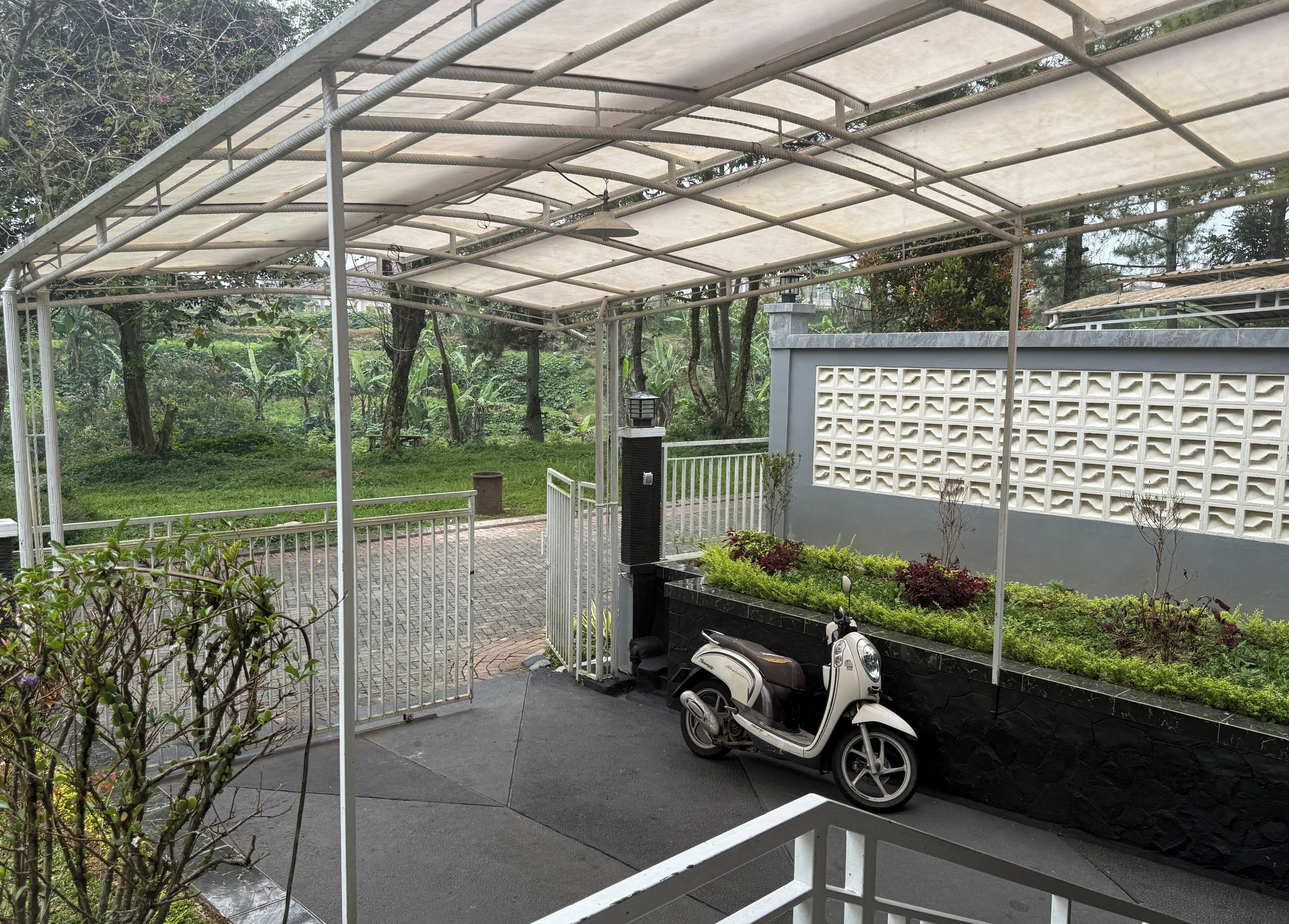Un espace extérieur abrité avec un scooter garé, un chemin pavé et un mur orné d’un motif texturé.