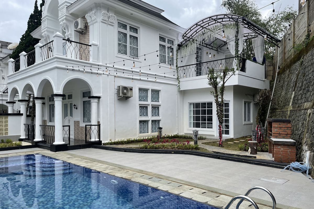 Un edificio grande de color blanco con piscina, balcones arqueados y un jardín.