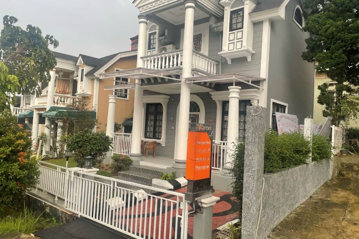 Una casa de dos pisos con balcón, entrada protegida por un portón y un cartel.