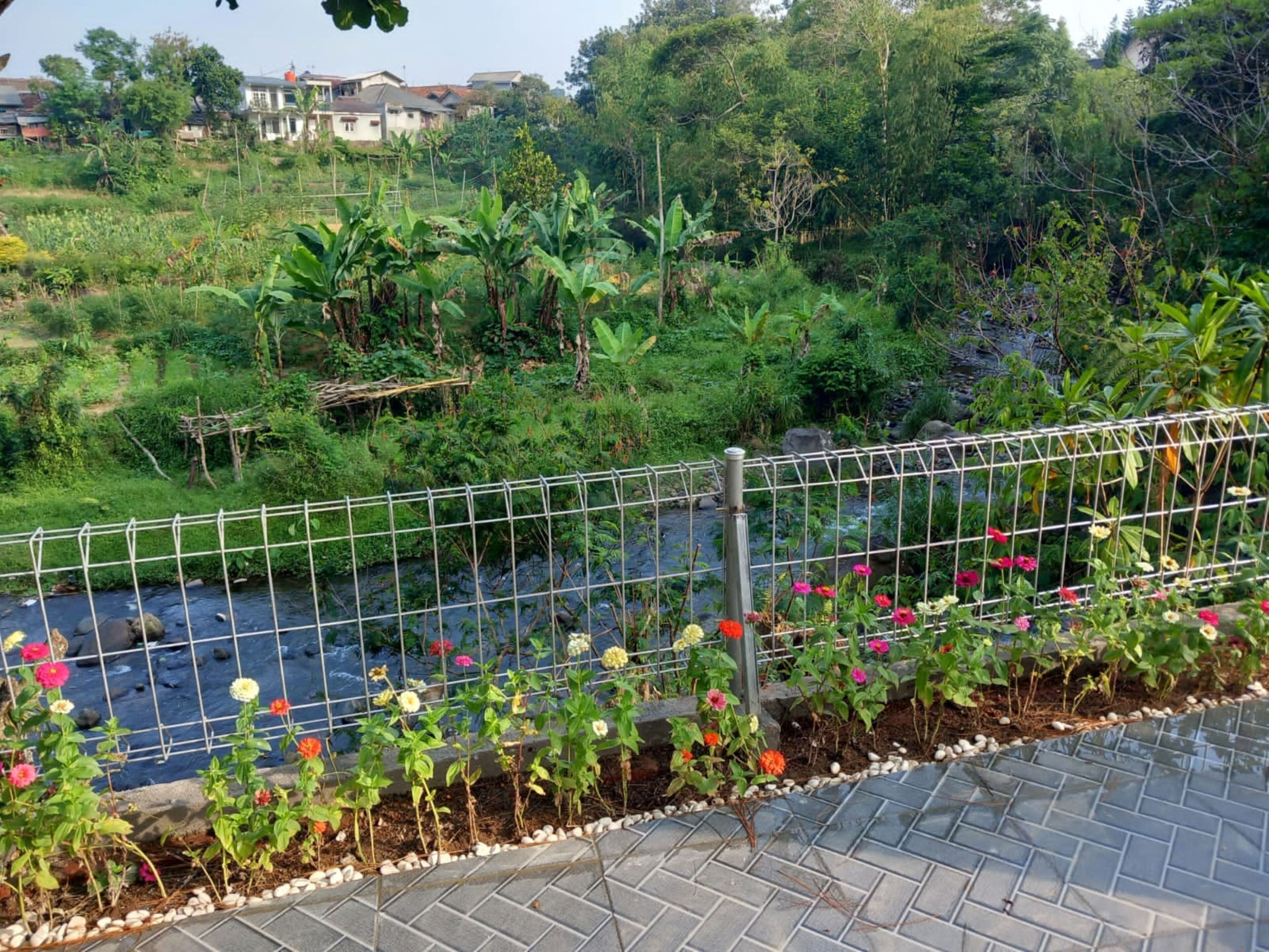 A garden with a water feature, surrounded by a metal fence, and a paved walkway.