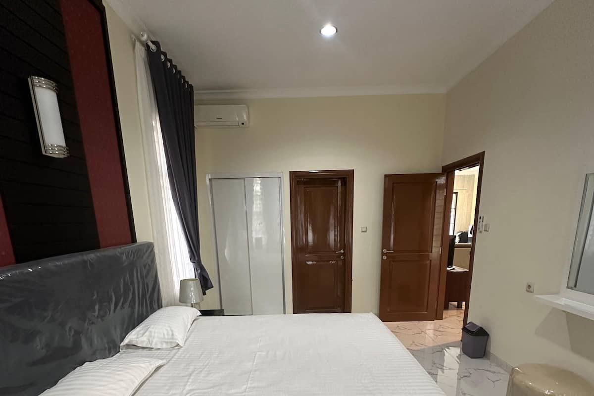 Un dormitorio con una cama grande, un armario, un espejo y un taburete pequeño.