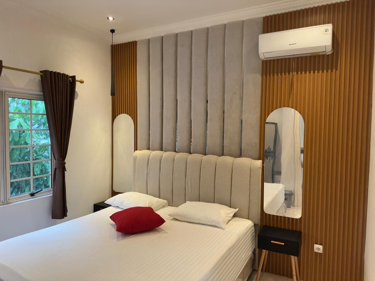 A bedroom with a large bed, a headboard, a mirror, and an air conditioning unit.