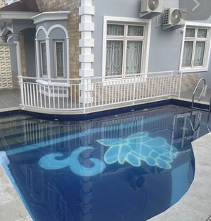 Ein Pool mit geometrischem Design, umgeben von einem weißen Zaun und einem Haus mit Steinverkleidung.