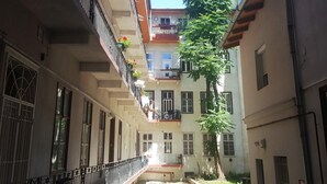 Un estrecho patio con un camino central flanqueado por edificios con balcones, barandillas y plantas en macetas.
