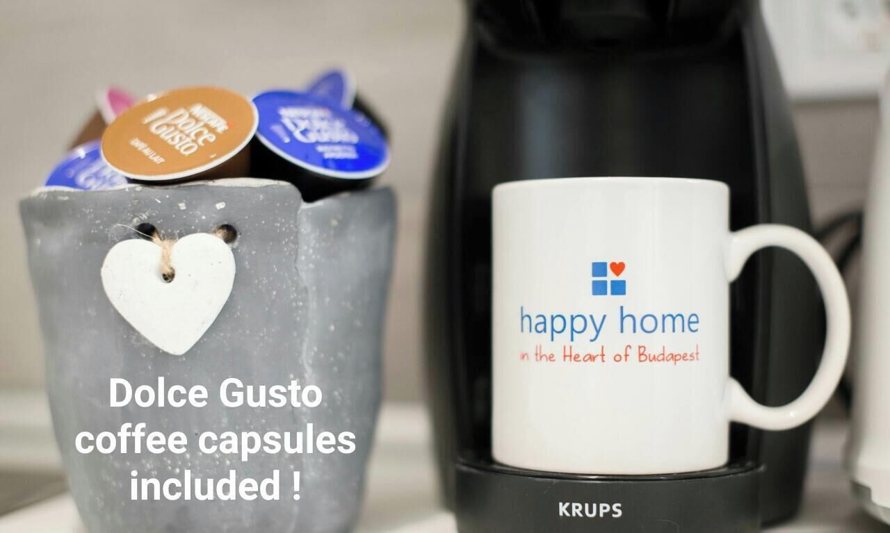 Une machine à café et une tasse ornée de l’inscription « un foyer heureux au cœur de Budapest », ainsi qu’un récipient en forme de cœur contenant des capsules de café.