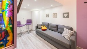 Una sala de estar moderna con un sofá gris, dos sillas moradas, una guitarra y un cuadro con mensajes motivacionales.