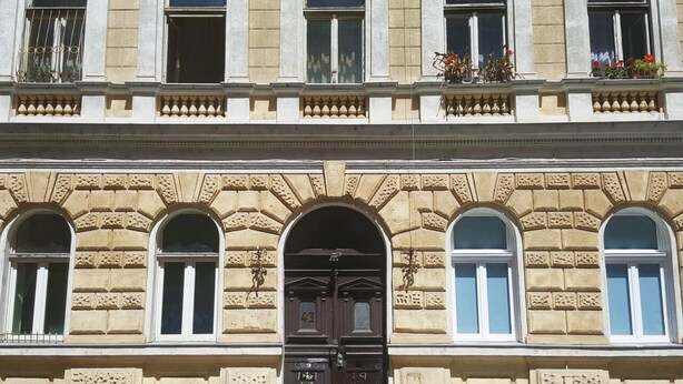 Un edificio con fachada simétrica, que presenta un arco central con puerta oscura, flanqueado por ventanas con marcos blancos.