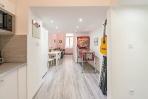 Um corredor estreito com uma cozinha à esquerda, uma sala de jantar com mesa e cadeiras, e um violão e um teclado à direita.