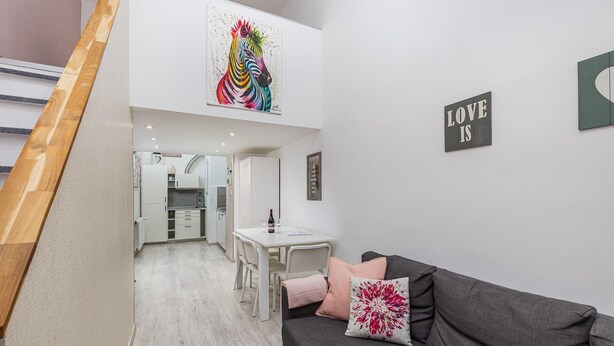 A modern apartment with a kitchen, dining area, and a living room with a grey sofa and a colorful painting. - happy home Budapest PINK   Central located apartment with 80  039 s pinball machine (Budapest)