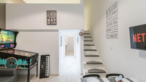 A modern living room with a piano, a pinball machine, and a dining area with a table set for two. - happy home Budapest DIAMOND Central located apartment with 80 039 s pinball machine (Budapest)
