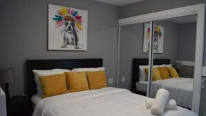 Hotelkamer met een groot bed, twee kussens, een witte deken, een spiegel en een schilderij van een hond aan de muur.