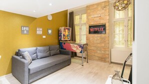 Uma sala de estar com um sofá cinza, um aviso da Netflix fixado na parede e uma placa com a palavra 'CASA' sobre uma janela.
