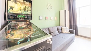 Una macchina da flipper in un soggiorno con un muro verde, un orologio e un divano grigio.