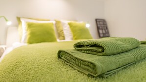 Un letto rifatto con biancheria e cuscini verdi, un asciugamano verde piegato sul letto e un lampadario fissato al muro.
