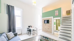Un soggiorno moderno con un tavolino in vetro, un divano con cuscini, un'area pranzo con tavolo e sedie, una cucina con parete in mattoni e un forno a microonde, e una scala con corrimano.