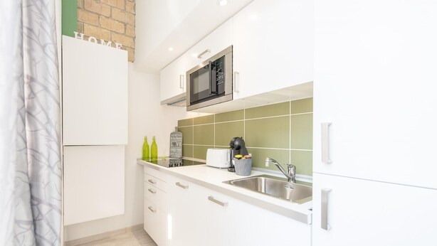 Una cucina moderna con mobili bianchi, un lavello in acciaio inossidabile e un forno a microonde.