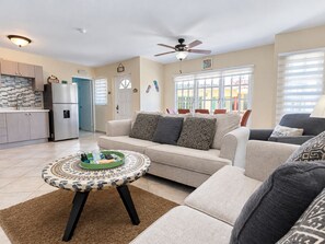 A living room with a sofa, a coffee table, and a kitchen area with a refrigerator.