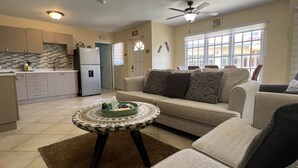 A modern living room with a beige sofa, a coffee table, and a kitchen area with cabinets and appliances.
