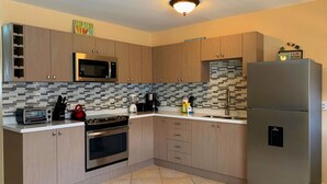 A modern kitchen with wooden cabinets, a stainless steel refrigerator, a microwave, a toaster, and a kettle.