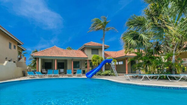 A swimming pool with a blue slide, lounge chairs, and palm trees.