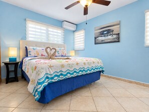 A bedroom with a bed, two bedside tables, a ceiling fan, and a painting on the wall.