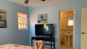 A bedroom with a bed, a television, a window, and a bathroom visible through an open door.