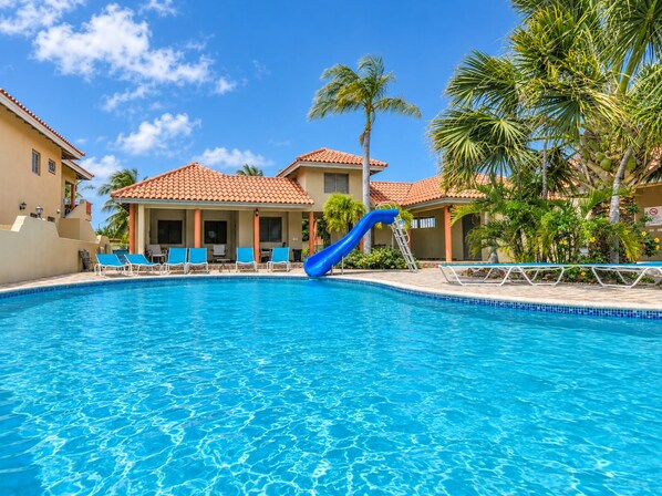 A swimming pool with a blue slide, lounge chairs, and palm trees.