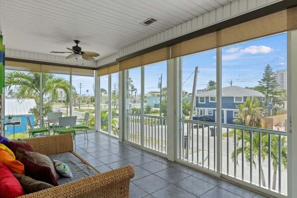 A room with a large window, a ceiling fan, a wicker sofa, and a view of the outside.