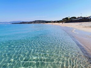 A clear beach with visible ripples in the water, a sandy shore, and a distant town.