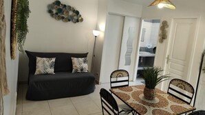 Ein Wohnzimmer mit einer Couch, einem Esstisch mit Stühlen, einer hängenden Pflanze und einem Wandbild.