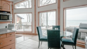 A kitchen with wooden cabinets, a microwave, and a dining area with chairs and a table. - Peak to Shore - Waterfront Cottage Located in Thornbury ON (Thornbury)