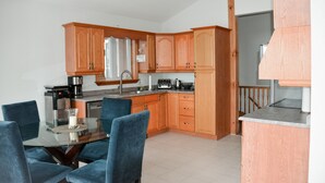 A modern kitchen with wooden cabinets, a dining table with chairs, and a coffee machine. - Peak to Shore - Waterfront Cottage Located in Thornbury ON (Thornbury)