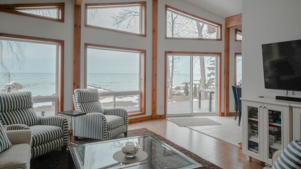 A spacious living room with large windows, a television, and a view of the sea. - Peak to Shore - Waterfront Cottage Located in Thornbury ON (Thornbury)