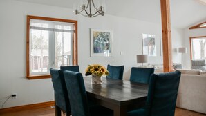 A dining area with a wooden table, blue chairs, and a vase of sunflowers. There are framed artworks on the walls and a chandelier above. - Peak to Shore - Waterfront Cottage Located in Thornbury ON (Thornbury)