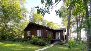 A wooden cabin with a stone pathway leading to the entrance, surrounded by lush greenery and trees. - Peak to Shore - Waterfront Cottage Located in Thornbury ON (Thornbury)