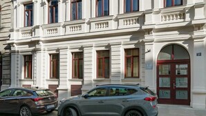 Un edificio de dos pisos con estilo arquitectónico clásico, que presenta un balcón con barandillas y una fachada simétrica con ventanas y puertas distribuidas uniformemente.