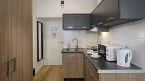 Una cocina compacta con armarios de madera, un lavamanos de acero inoxidable, una estufa y un hervidor.