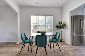 Une cuisine moderne avec un réfrigérateur en acier inoxydable, une table à manger entourée de chaises de couleur turquoise et une grande fenêtre donnant sur l’extérieur.