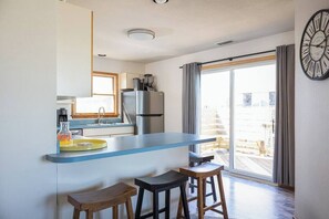 A modern kitchen with a blue countertop, a refrigerator, and a sink. There are two stools and a bench. - 1-Min walk to Beach! Ocean Views, Hot Tub (Corolla)