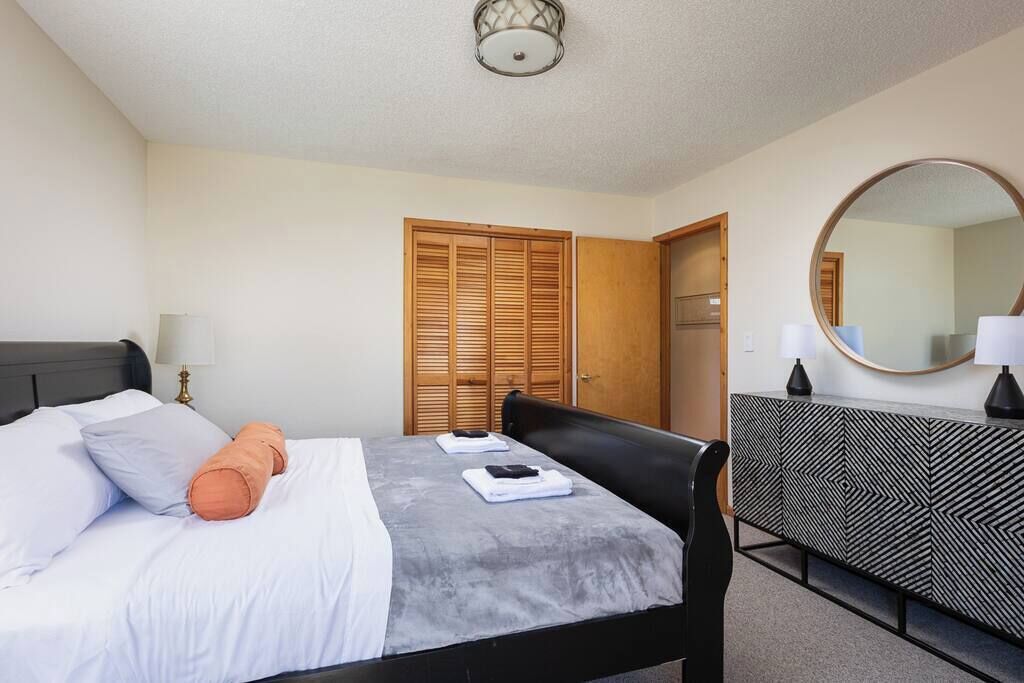 A hotel room with a bed, a bedside table with a lamp, a wardrobe, and a mirror on the wall.